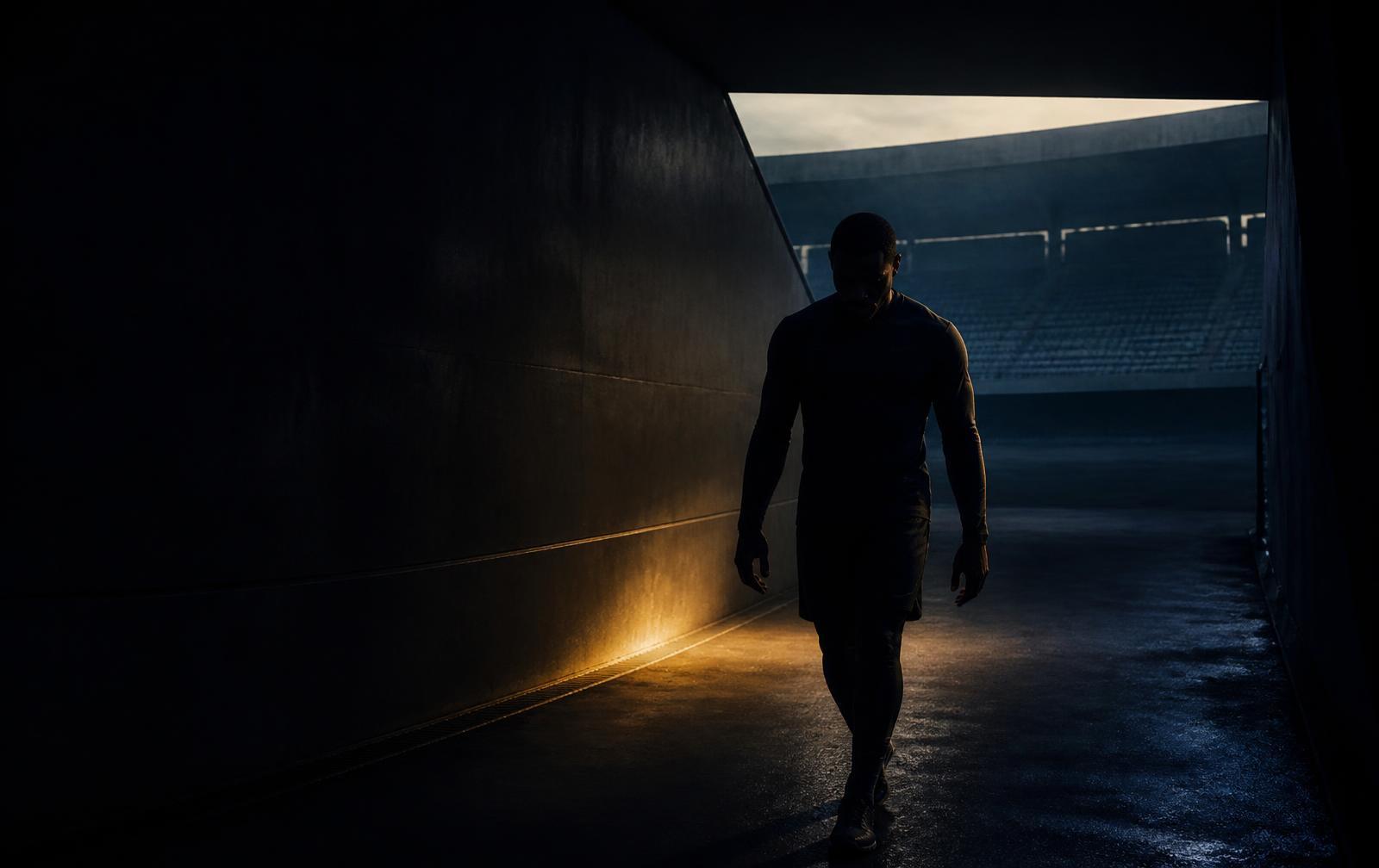 An athlete walking through a dark stadium tunnel at dawn